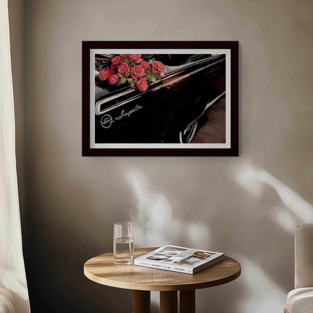 Framed artwork of a car with flowers on a wall above a wooden table with a glass and magazine.