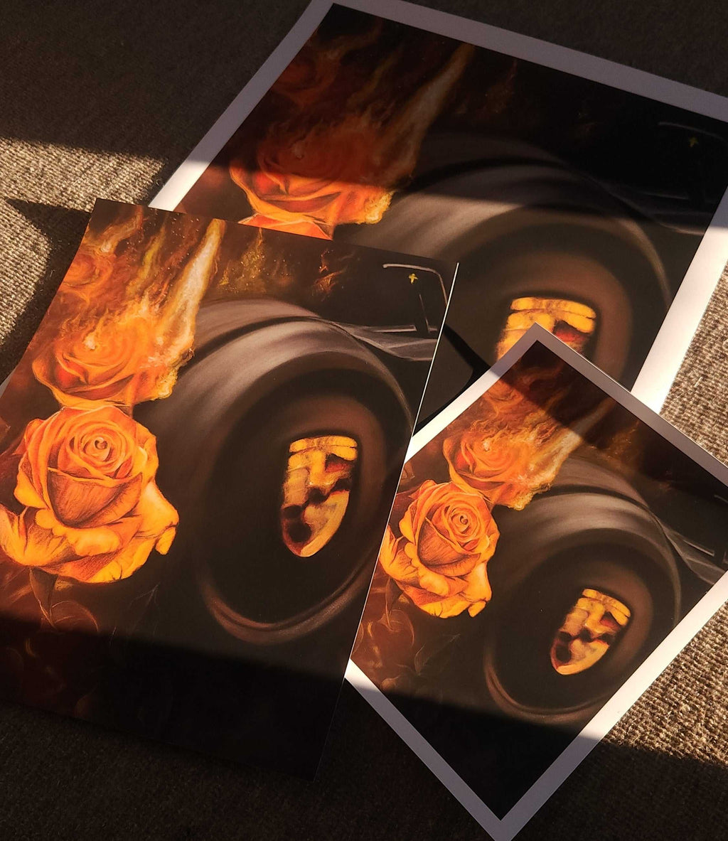 Three printed art photos or posters laid on a textured dark surface, showing a stylized fiery orange and yellow rose and Porsche steering wheel