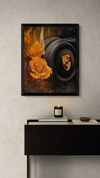 A framed art print featuring a dark camera lens and a glowing orange rose with flames, displayed on a textured light gray wall above a dark console table with a candle and books.