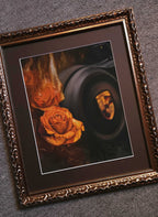 A framed art print featuring a dark, moody painting with two orange roses and a hooded face, presented in an ornate gold frame against a textured gray background.
