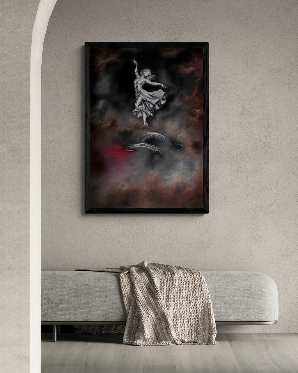 A framed vertical art print featuring a white dancing figure against a dark smoky background with red accents, displayed on a light gray wall above a modern gray bench with a textured throw blanket.