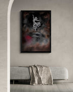 A framed vertical art print featuring a white dancing figure against a dark smoky background with red accents, displayed on a light gray wall above a modern gray bench with a textured throw blanket.