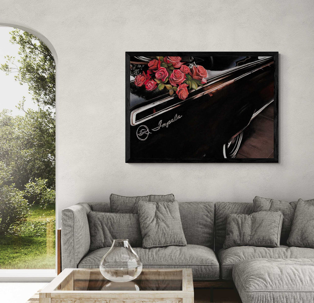 A framed wall art print depicting red roses on a black car door with the word 'Impala' visible, displayed above a gray sectional sofa in a modern living room setting.