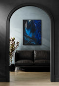 A framed abstract art print featuring vibrant blue and black fluid patterns, displayed on a light gray wall above a black leather sofa in a modern living room setting.